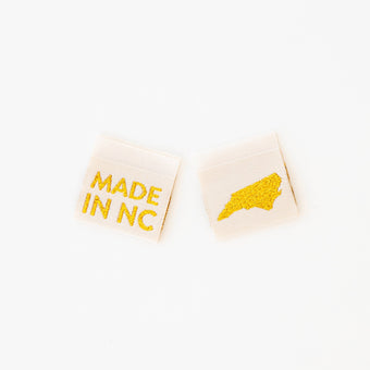 woven sew in labels by Sarah hearts with 'MADE IN NC' text and a North Carolina outline in gold metallic on a cream background