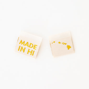 woven sew in labels by Sarah Hearts with 'MADE IN HI' text and an outline of the Hawaiian Islands in gold metallic thread on a white background