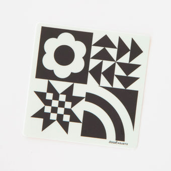 A sticker with a black and white quilt block design, including geometric shapes and a flower.