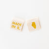 woven sew in labels by Sarah Hearts with 'MADE IN IL' text and an outline of the state of Illinois in gold metallic thread on a white background.