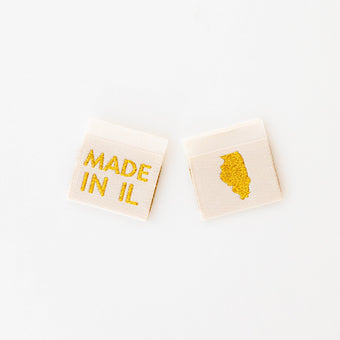 woven sew in labels by Sarah Hearts with 'MADE IN IL' text and an outline of the state of Illinois in gold metallic thread on a white background.