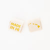 woven sew in labels by Sarah Hearts with 'MADE IN HI' text and an outline of the Hawaiian Islands  in gold metallic thread on a white background