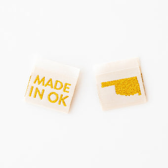 woven sew in labels by Sarah hearts with 'MADE IN OK' text and Oklahoma state outline in gold metallic on a cream background