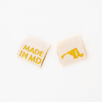 woven sew in labels by Sarah Hearts with 'MADE IN MD' text and an outline of the state of Maryland in gold metallic thread on a white background.